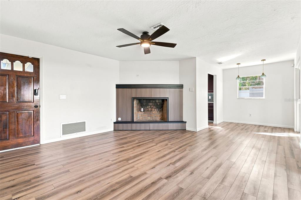 A living room features light wood-look flooring, a brick fireplace, and sliding glass patio doors — 1441 NE OLD MILL DRIVE, DELTONA, FL