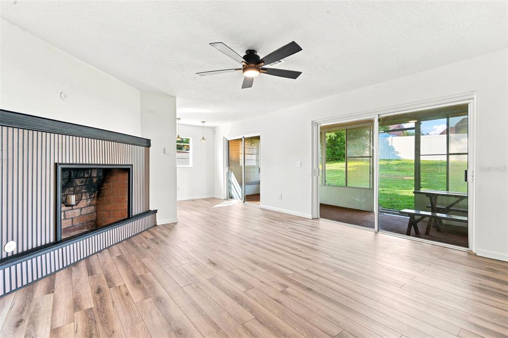 A living room features wood-look flooring, a ceiling fan, and a fireplace with wood paneling — 1441 NE OLD MILL DRIVE, DELTONA, FL