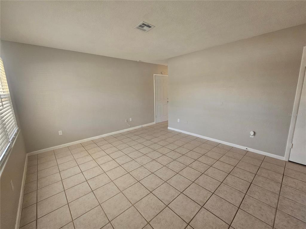 An empty room features beige walls, light-colored tile flooring, and a white door — 7000 BRENTFORD ROAD, SARASOTA, FL