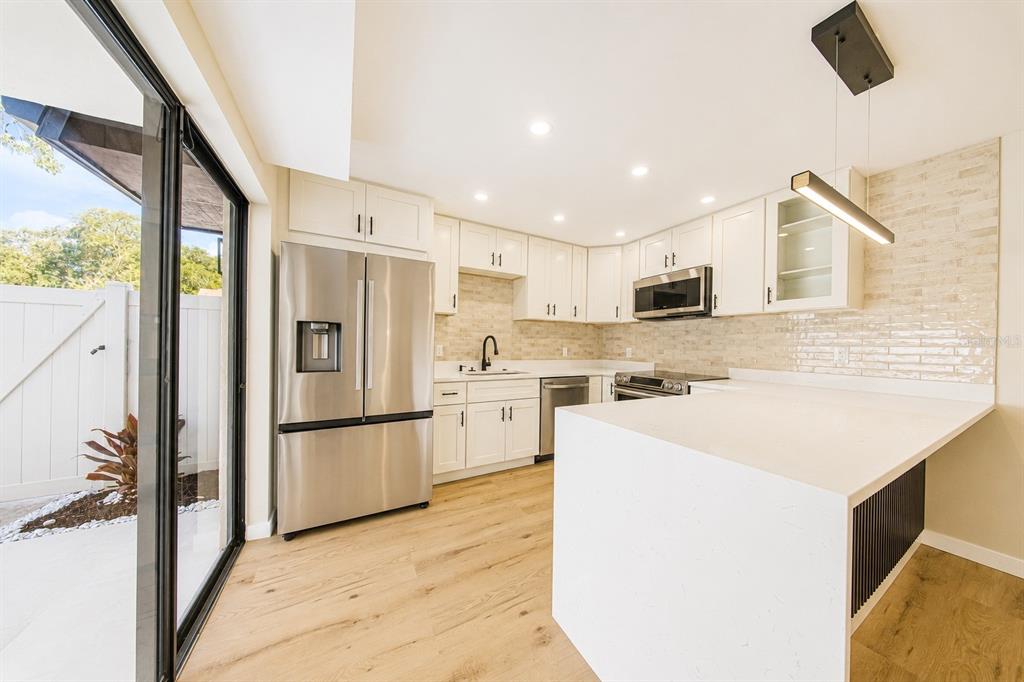 A modern kitchen features white cabinets, stainless steel appliances, a quartz island, and light flooring — 4030 SHANNON BROWN DRIVE, ORLANDO, FL