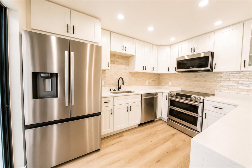 A modern kitchen features white cabinets, stainless steel appliances, and a light-colored tile backsplash — 4030 SHANNON BROWN DRIVE, ORLANDO, FL
