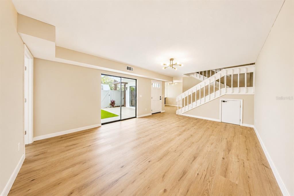An empty living room features light wood-look flooring, a staircase, and a sliding glass door — 4030 SHANNON BROWN DRIVE, ORLANDO, FL