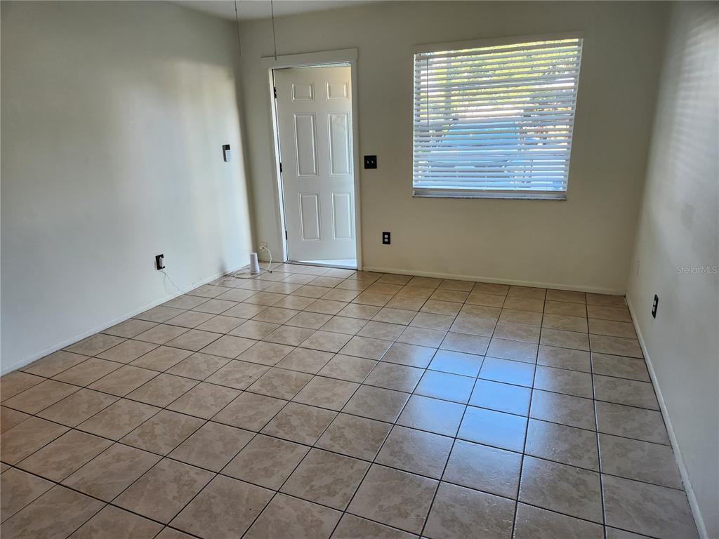 An empty room with beige tile flooring, white walls, a window with blinds, and a door — 1120 36TH STREET W UNIT A, BRADENTON, FL