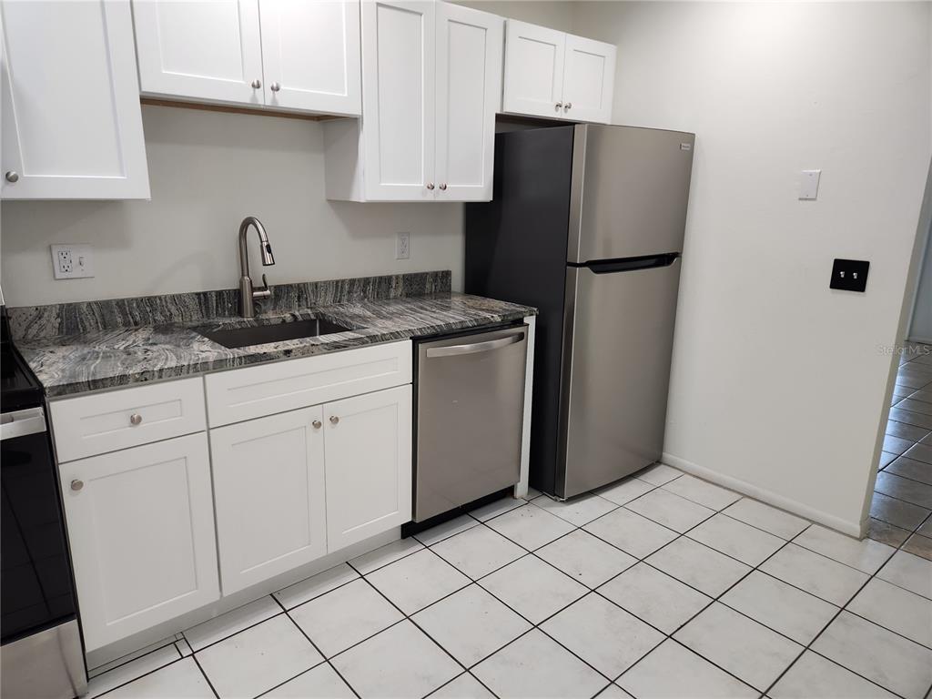 A kitchen features white cabinets, granite countertops, stainless steel appliances, and white tiled flooring — 1120 36TH STREET W UNIT A, BRADENTON, FL