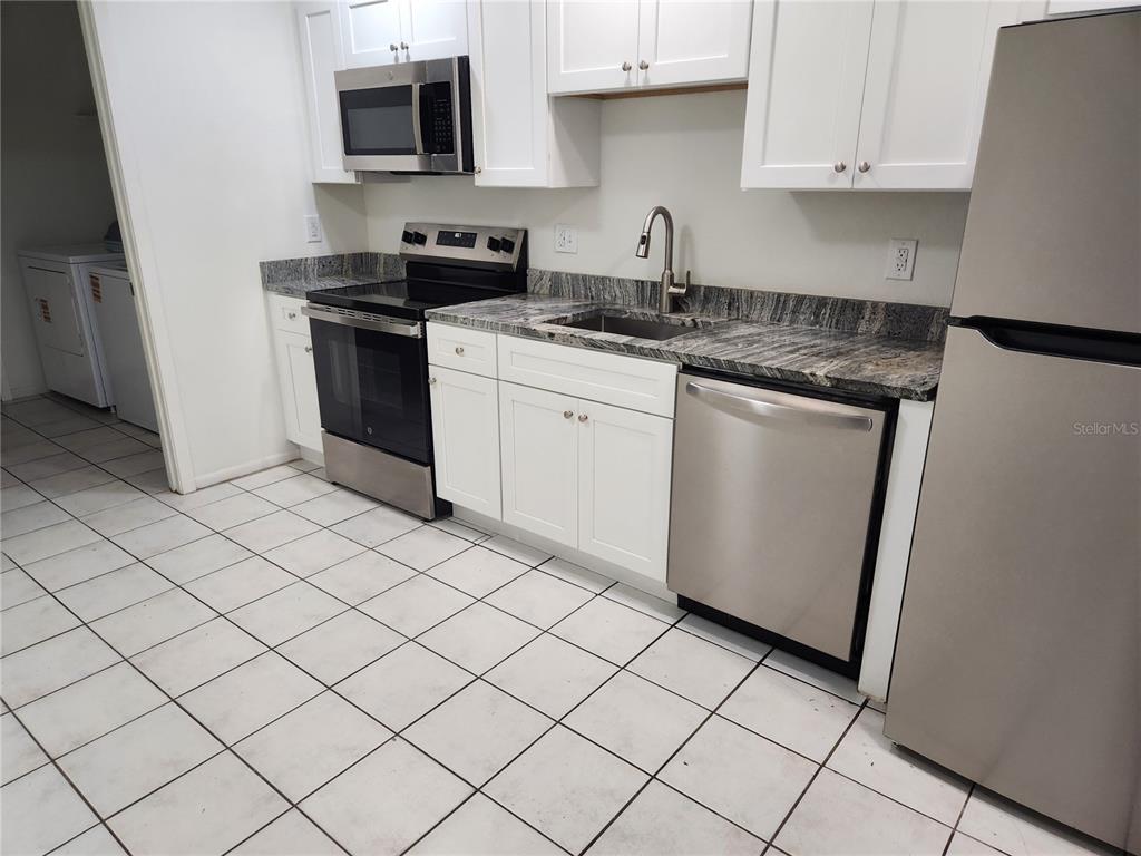 A kitchen features white cabinets, stainless steel appliances, and dark granite countertops over tiled floors — 1120 36TH STREET W UNIT A, BRADENTON, FL