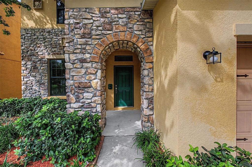 A stone-arched entryway leads to a dark green front door on a stucco house — 440 WESTCHESTER HILLS LANE, VALRICO, FL