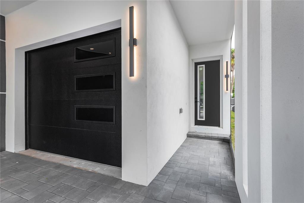 A modern home exterior features a black garage door, a matching front door, and stone pavers — 6021 INTERBAY UNIT 1, TAMPA, FL