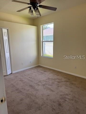 A bedroom with beige carpet, a ceiling fan, and a window overlooking a neighboring house — 3321 PAWLEYS LOOP N, ST CLOUD, FL