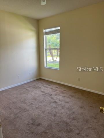 An empty bedroom with beige walls, brown carpet, and a single window overlooking trees — 3321 PAWLEYS LOOP N, ST CLOUD, FL