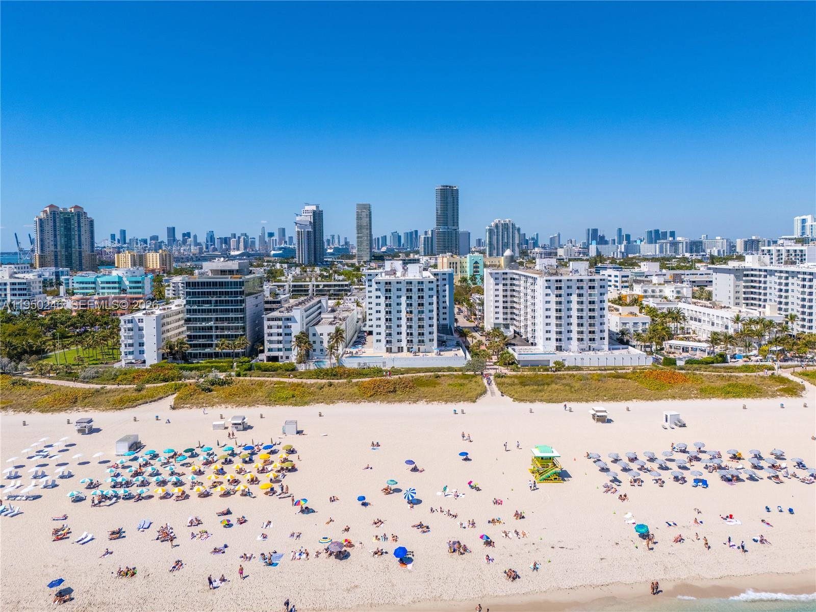 An aerial view shows a sandy beach with umbrellas and people in front of coastal buildings — 345 Ocean Dr # 610, Miami Beach FL 33139, MIAMI BEACH, FL