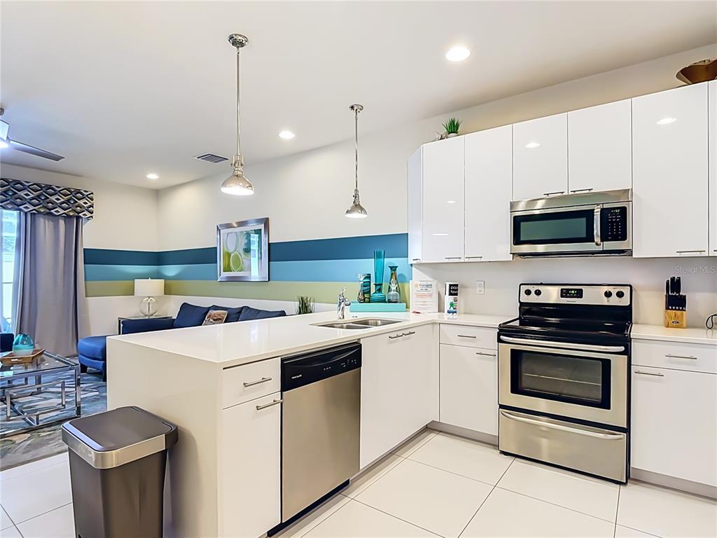 A modern kitchen features white cabinets, stainless steel appliances, and a white quartz island — 1433 RETREAT CIR, CLERMONT, FL