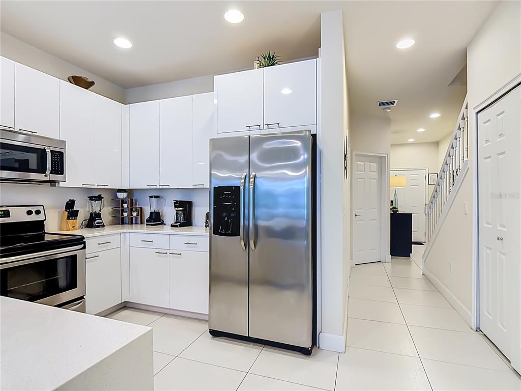 A modern kitchen features white glossy cabinets, stainless steel appliances, and light tile flooring — 1433 RETREAT CIR, CLERMONT, FL