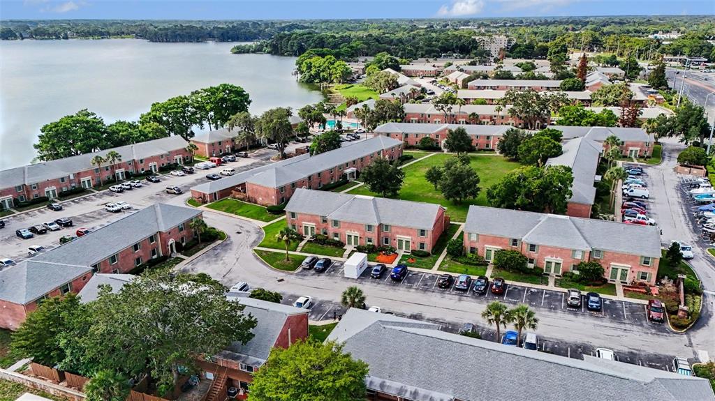 An aerial view shows multiple brick apartment buildings with gray roofs surrounding a central lawn — 120 GEORGETOWN DRIVE UNIT 120, CASSELBERRY, FL