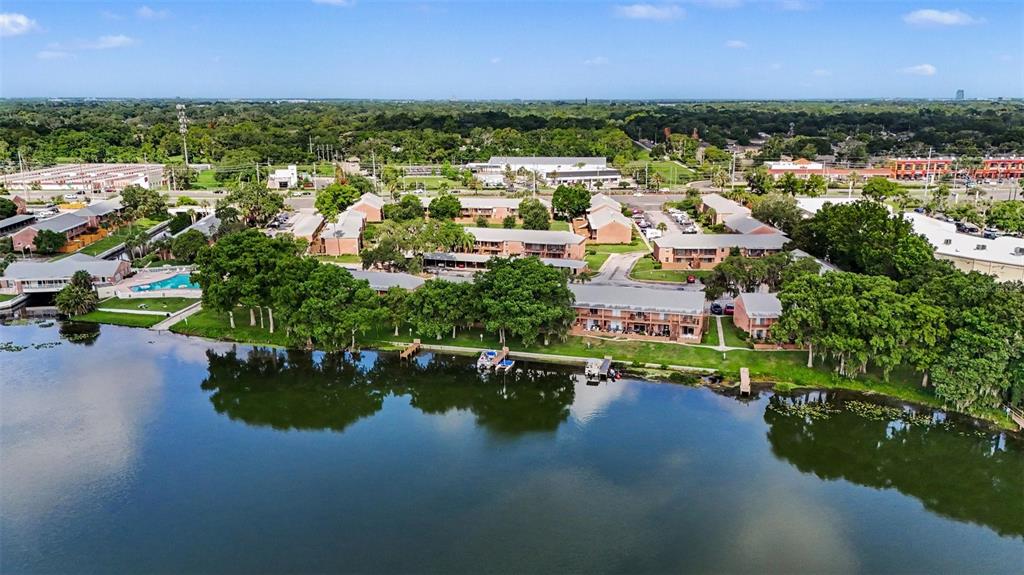 An aerial view shows apartment buildings situated along the edge of a large lake — 120 GEORGETOWN DRIVE UNIT 120, CASSELBERRY, FL