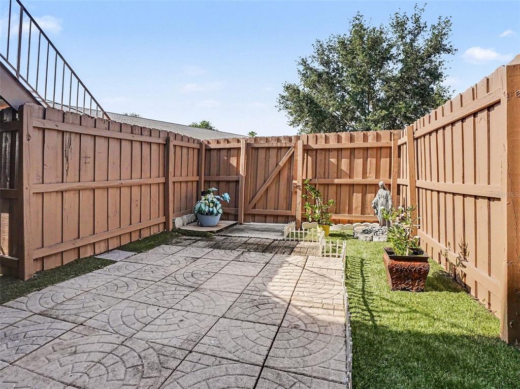A fenced-in backyard patio features concrete pavers, a small patch of grass, and potted plants — 120 GEORGETOWN DRIVE UNIT 120, CASSELBERRY, FL
