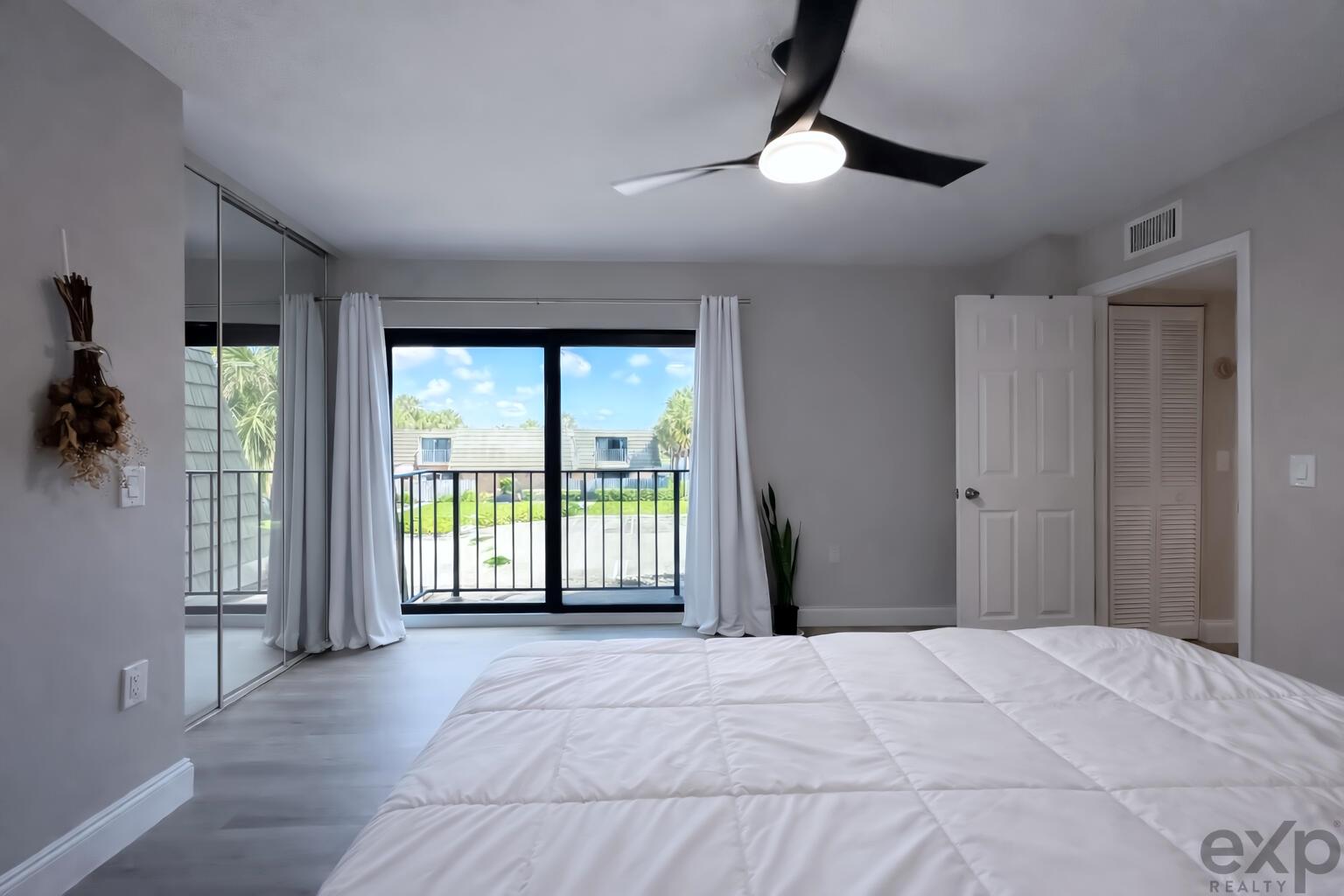 A bedroom features light gray flooring, a ceiling fan, mirrored closet doors, and a balcony — 1008 10th Way, West Palm Beach FL 33407, WEST PALM BEACH, FL