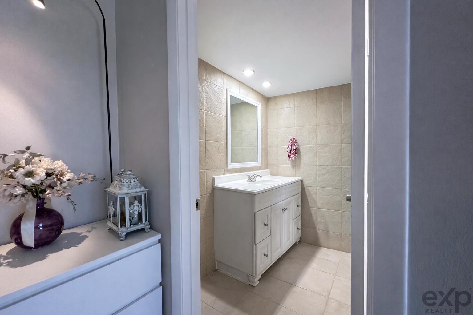 A bathroom with a white vanity, tiled walls, and a mirror viewed through a doorway — 1008 10th Way, West Palm Beach FL 33407, WEST PALM BEACH, FL