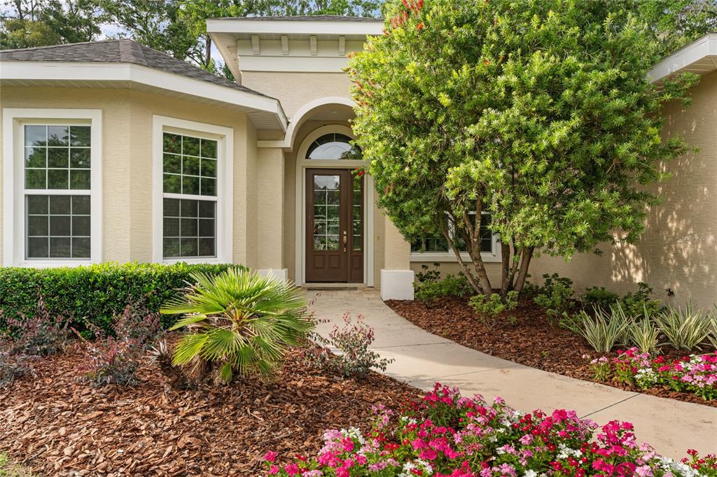 A beige house exterior features a front door with a glass transom and landscaping — 4117 SE 21ST STREET, OCALA, FL