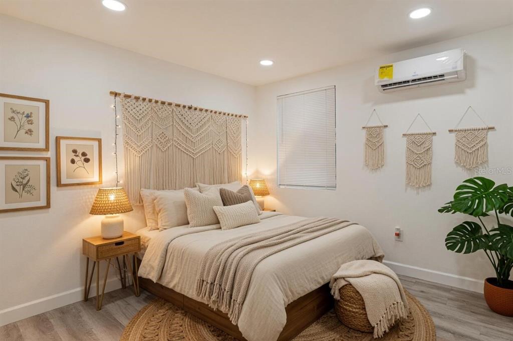 A bedroom features a macramé headboard, neutral bedding, a round rug, and a wall-mounted air conditioner — 57 CABANA AVENUE, NORTH FORT MYERS, FL