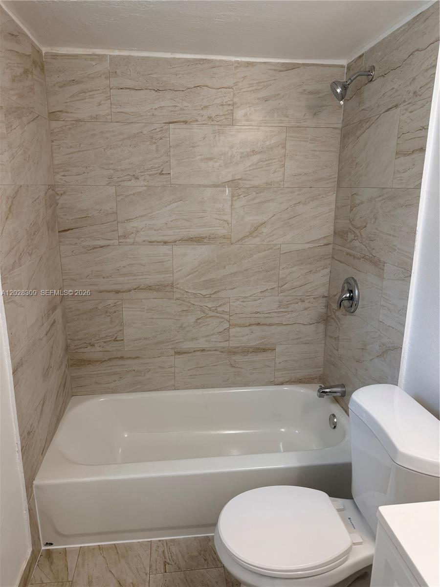 A bathroom features a white bathtub with a showerhead and beige stone-look tile walls — 220 NW 16th Ter # 1, Miami FL 33136, MIAMI, FL
