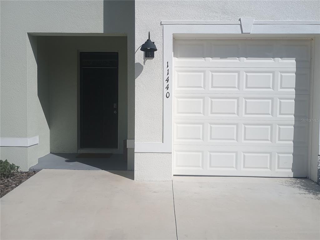 The exterior of a home features a white garage door and a recessed front entrance — 11440 CRESCENT DEER DRIVE, LAND O LAKES, FL