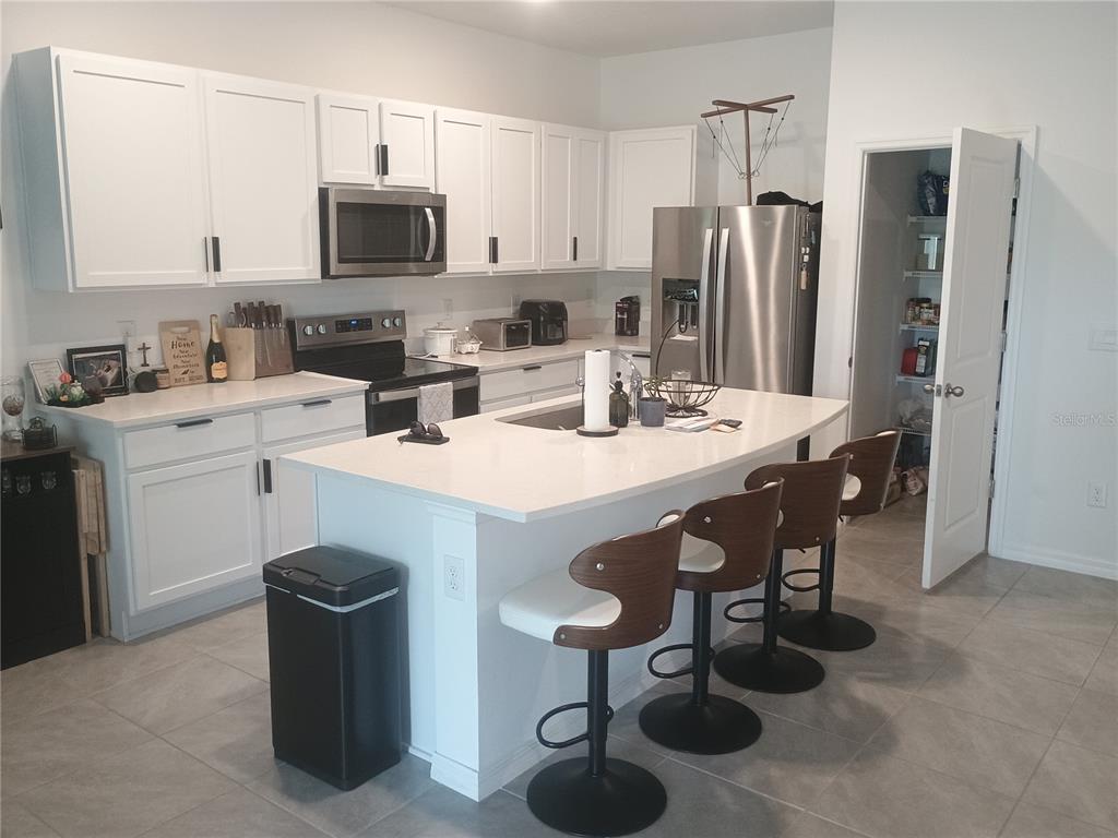 A kitchen features white cabinets, stainless steel appliances, a center island with barstools, and a pantry — 11440 CRESCENT DEER DRIVE, LAND O LAKES, FL
