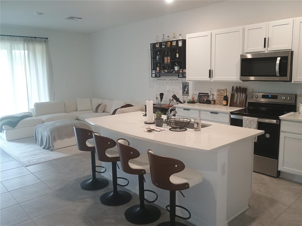 A kitchen with a white island and bar stools opens to a living area — 11440 CRESCENT DEER DRIVE, LAND O LAKES, FL