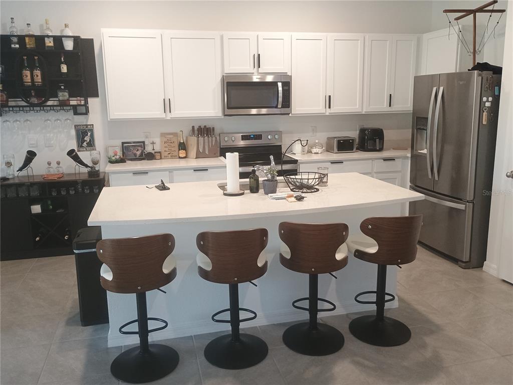 A kitchen features white cabinets, stainless steel appliances, a quartz island, and four bar stools — 11440 CRESCENT DEER DRIVE, LAND O LAKES, FL
