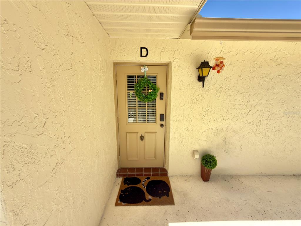 A tan front door with a wreath and a cat-themed doormat under a porch light — 1333 SHADY PINE WAY UNIT D, TARPON SPRINGS, FL