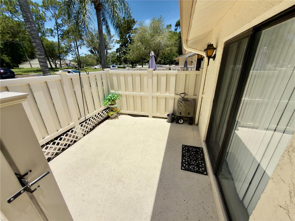 A concrete patio features a white privacy fence, a sliding glass door, and a doormat — 1333 SHADY PINE WAY UNIT D, TARPON SPRINGS, FL