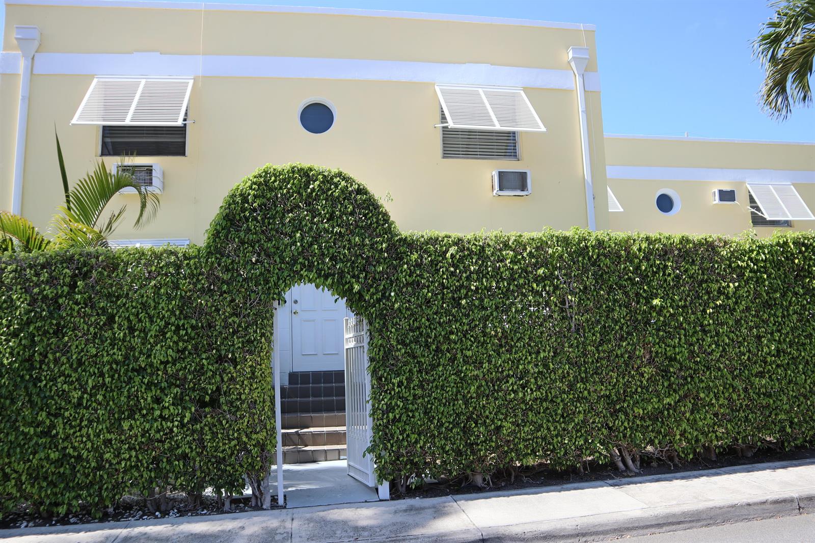 A yellow building with white shutters and a circular window behind a tall hedge archway — 172 N County Road, Palm Beach FL 33480, PALM BEACH, FL