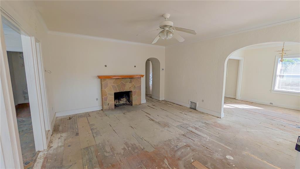 An empty living room features a stone fireplace, arched doorways, and unfinished wood flooring — 852 4TH AVENUE N, ST PETERSBURG, FL