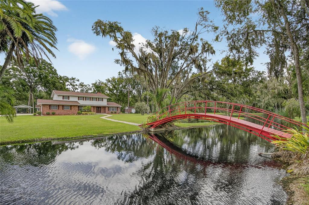 A red arched bridge spans a pond in front of a two-story brick house — 1502 AZALEA STREET, PLANT CITY, FL