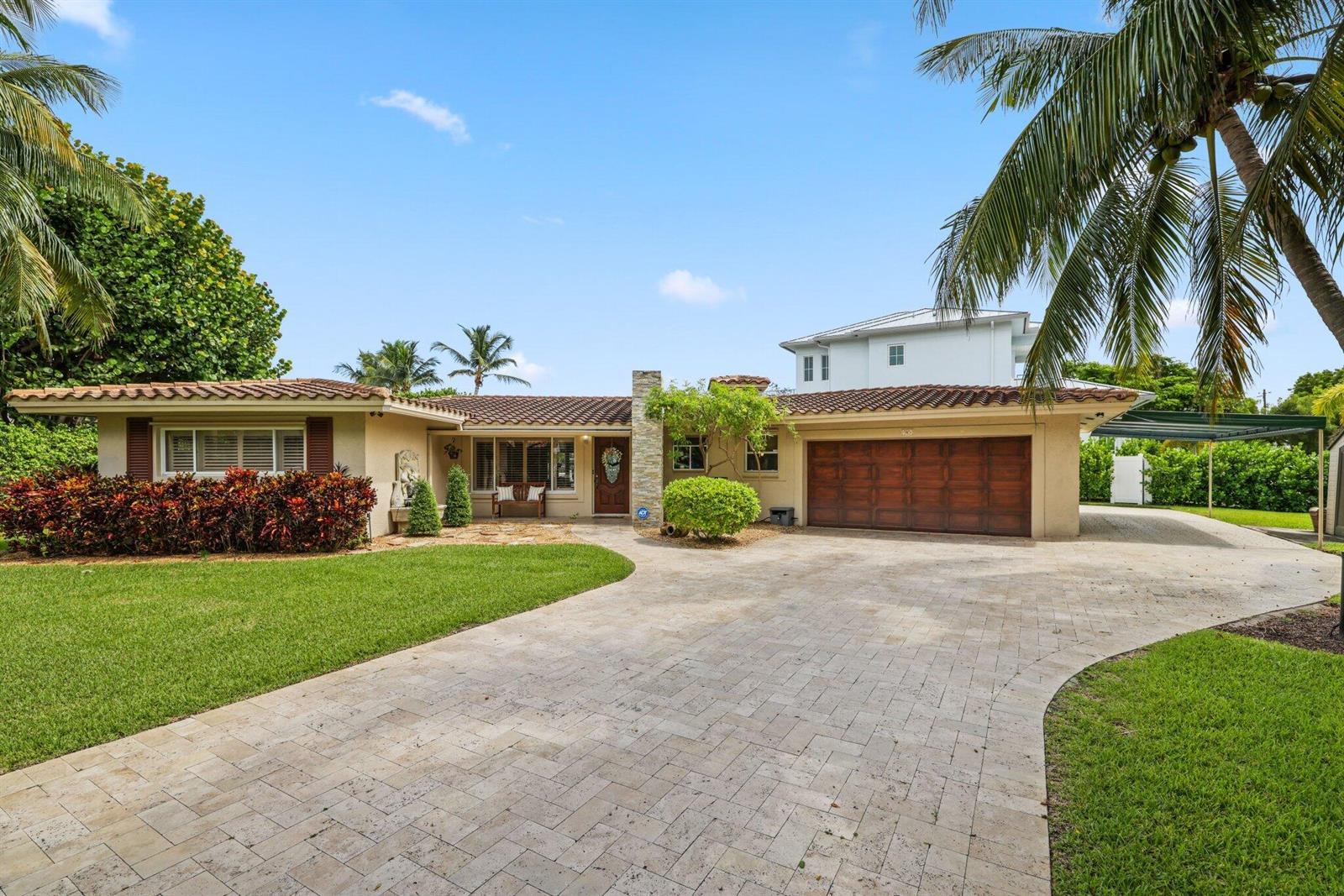 A single-story house with a tiled roof, stone chimney, and a paved driveway — 910 Banyan Drive, Delray Beach FL 33483, DELRAY BEACH, FL