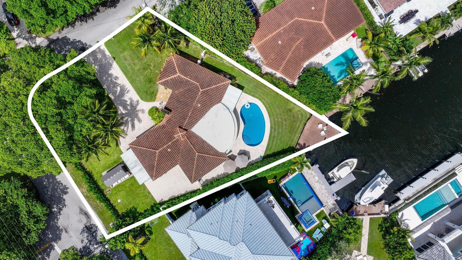 An aerial view shows a house with a tiled roof, pool, and lawn on a canal — 910 Banyan Drive, Delray Beach FL 33483, DELRAY BEACH, FL