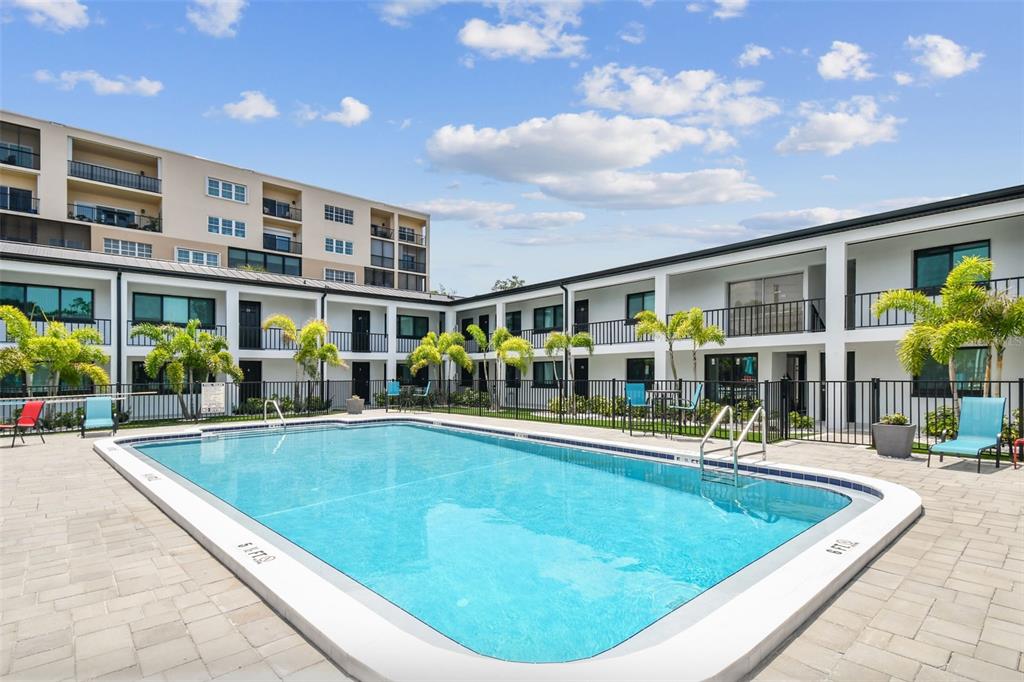 A rectangular swimming pool sits in a courtyard surrounded by two-story apartment buildings and palm trees — 2942 W BAY DRIVE UNIT 33, BELLEAIR BLUFFS, FL