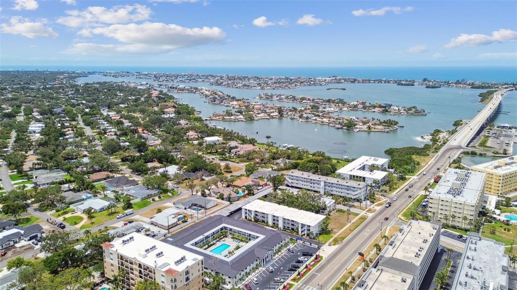An aerial view shows a coastal neighborhood with apartment complexes, a bridge, and surrounding water — 2942 W BAY DRIVE UNIT 33, BELLEAIR BLUFFS, FL