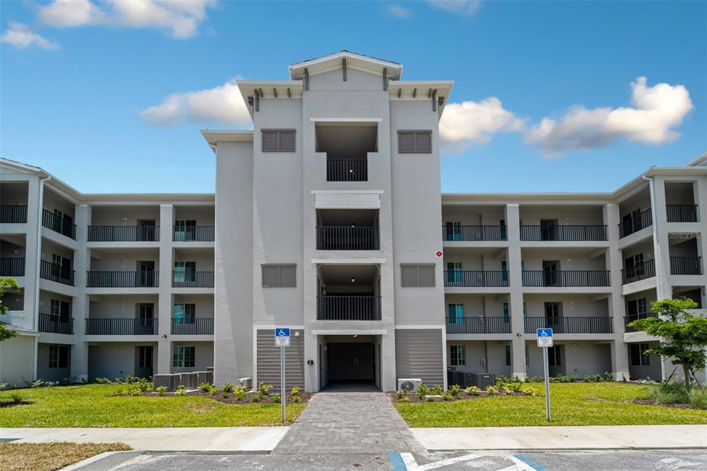 A multi-story apartment building with a central entrance, balconies, and a paved walkway — 12280 WELLEN GOLF STREET UNIT 105, VENICE, FL
