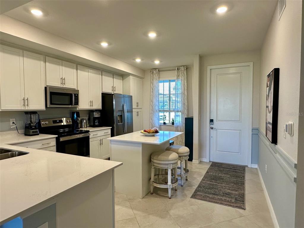 A kitchen features white cabinetry, stainless steel appliances, a center island, and tile flooring — 12280 WELLEN GOLF STREET UNIT 105, VENICE, FL
