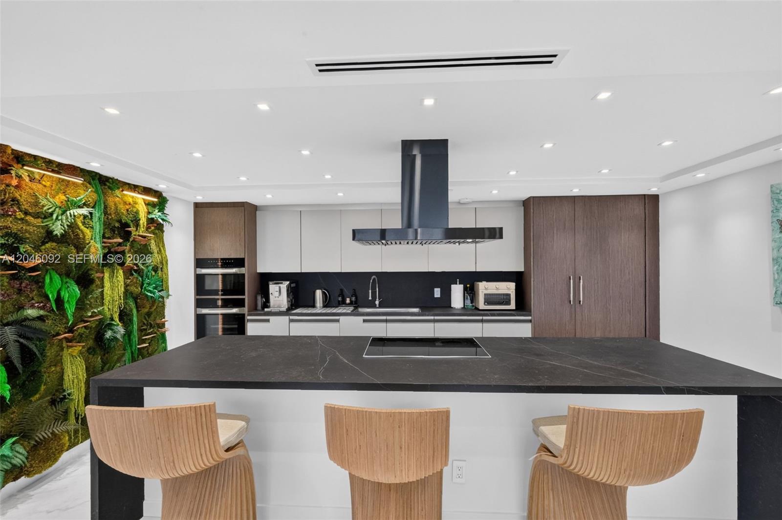 A modern kitchen features a large black island, wooden bar stools, and a living wall — 2301 Collins Ave # 443, Miami Beach FL 33139, MIAMI BEACH, FL
