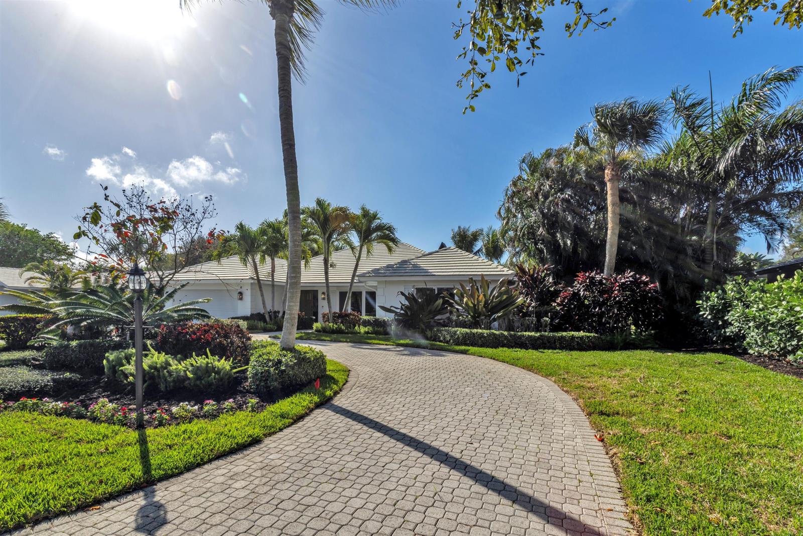 A single-story house with a paved driveway and lush tropical landscaping under a sunny sky — 2720 Cardinal Circle, Gulf Stream FL 33483, GULF STREAM, FL