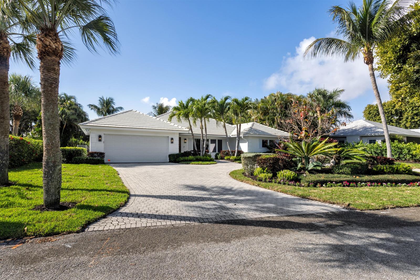 A white single-story house with a paved driveway and palm trees under a blue sky — 2720 Cardinal Circle, Gulf Stream FL 33483, GULF STREAM, FL