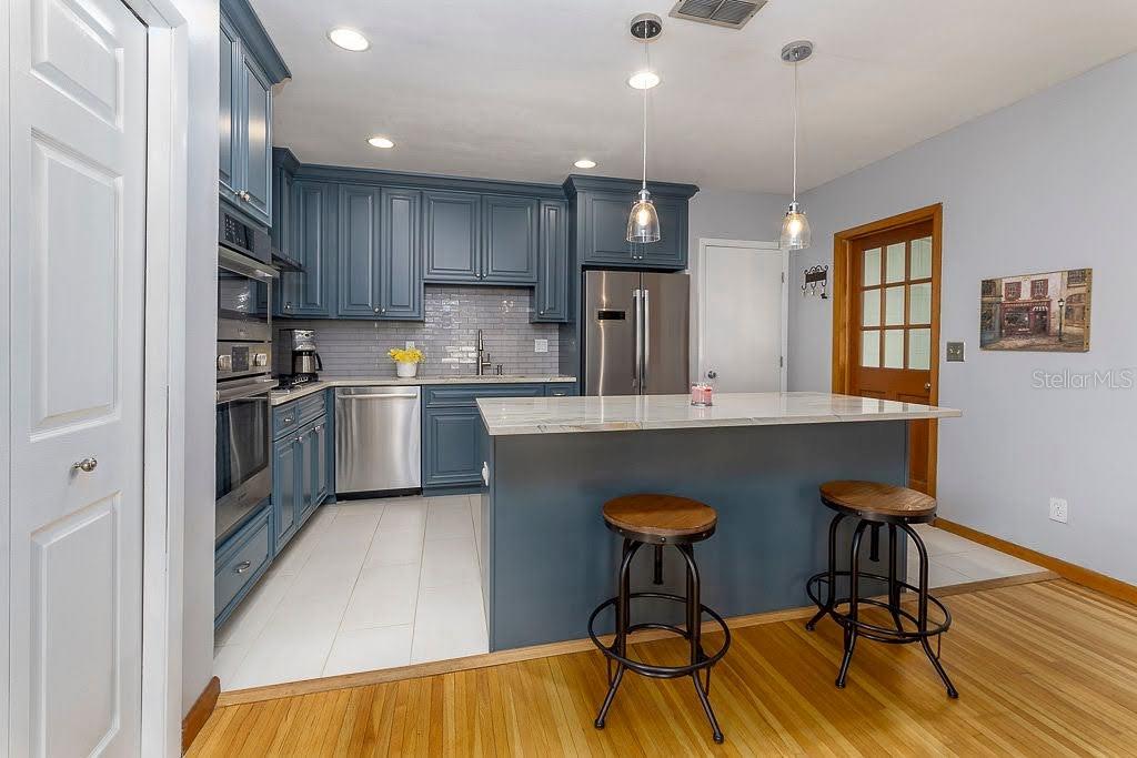 A kitchen features blue cabinets, stainless steel appliances, a marble-topped island, and hardwood flooring — 11 S UNIVERSITY CIRCLE, DELAND, FL