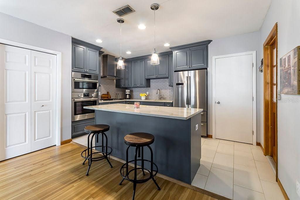 A kitchen features dark gray cabinets, stainless steel appliances, a central island, and wood flooring — 11 S UNIVERSITY CIRCLE, DELAND, FL