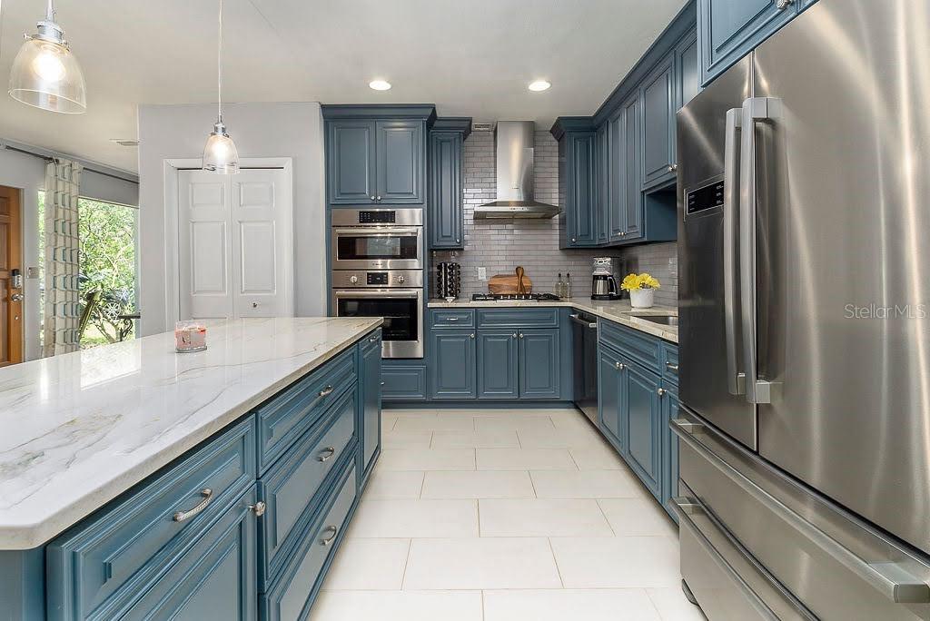 A kitchen features blue cabinets, stainless steel appliances, a marble-topped island, and light tile flooring — 11 S UNIVERSITY CIRCLE, DELAND, FL