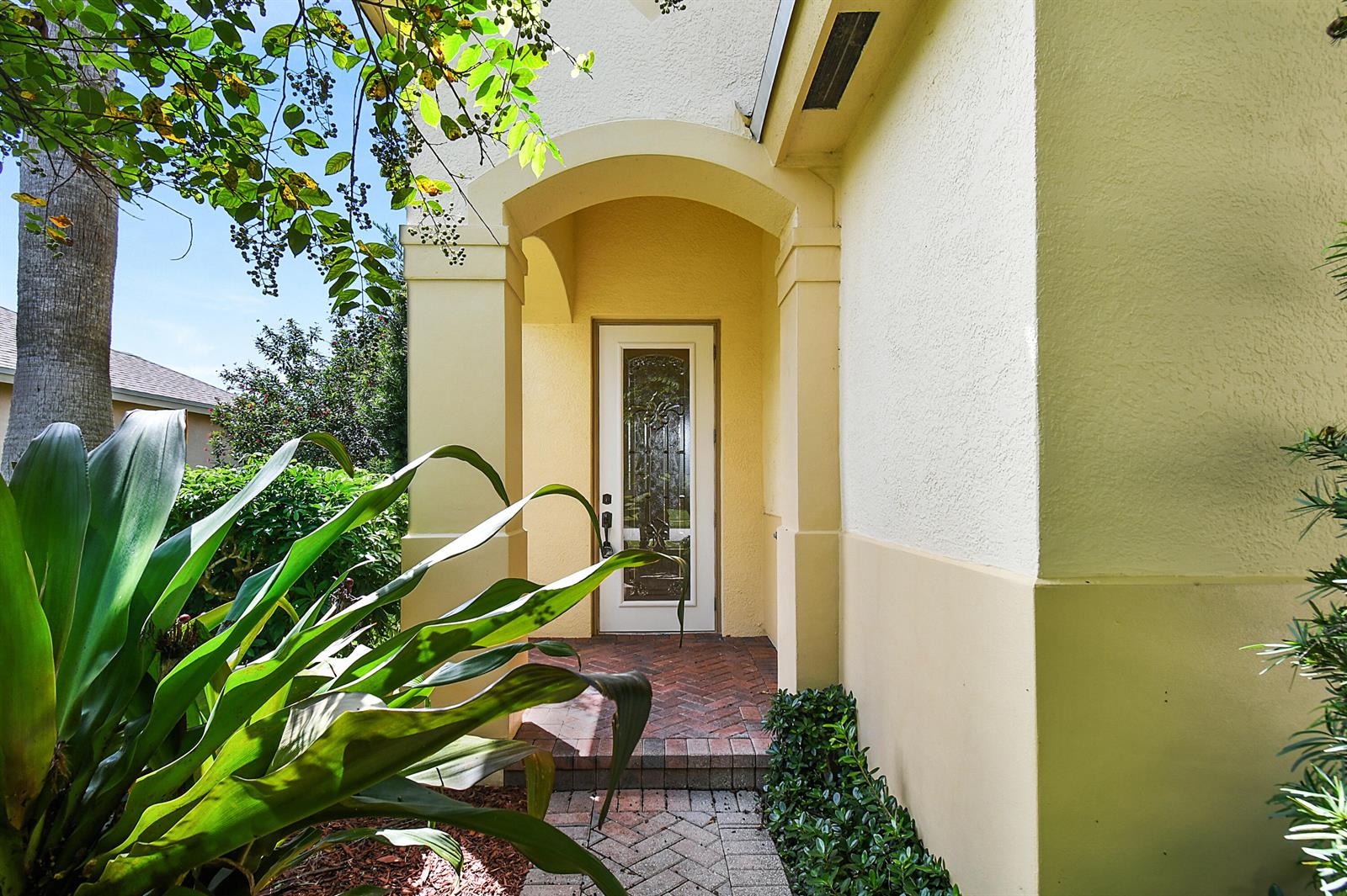 A front entrance with a glass-paneled door, brick walkway, and stucco walls under an archway — 9902 E Verona Circle Circle, Vero Beach FL 32966, VERO BEACH, FL