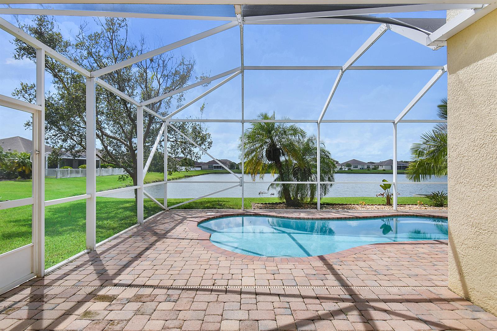 A screened-in patio features a brick paver deck, a swimming pool, and a lake view — 9902 E Verona Circle Circle, Vero Beach FL 32966, VERO BEACH, FL
