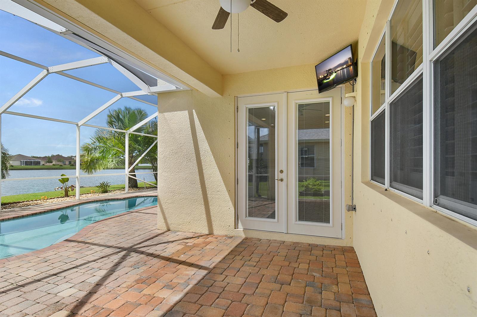 A covered patio features brick pavers, a ceiling fan, a wall-mounted television, and a pool — 9902 E Verona Circle Circle, Vero Beach FL 32966, VERO BEACH, FL