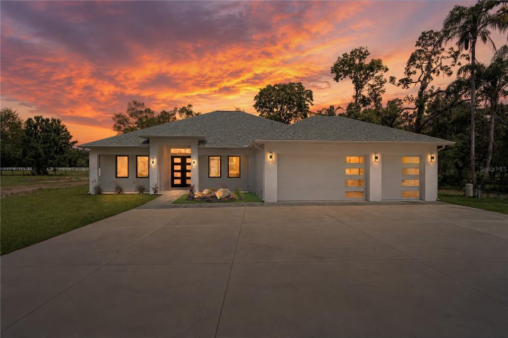 A modern single-story house with a two-car garage at sunset — 10928 OSCEOLA DRIVE, NEW PORT RICHEY, FL