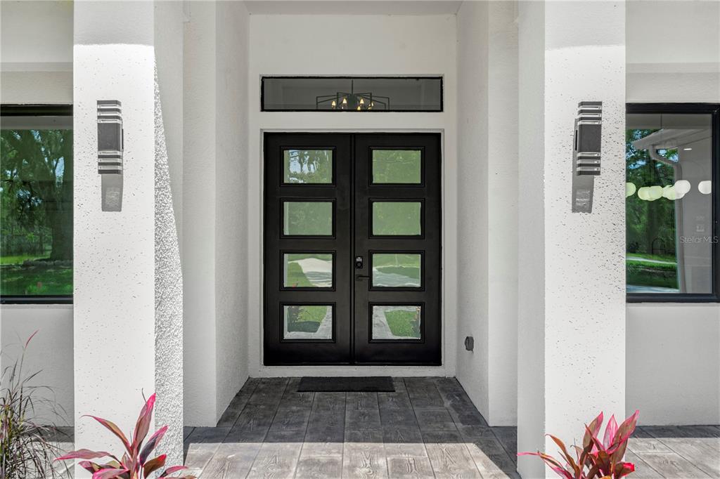 A modern entryway features double black doors with glass panels between two white pillars — 10928 OSCEOLA DRIVE, NEW PORT RICHEY, FL